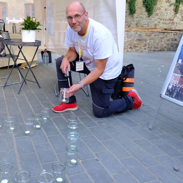 Ein Mann kniet auf der Straße und zündet eine Kerze in einem Glas an.
