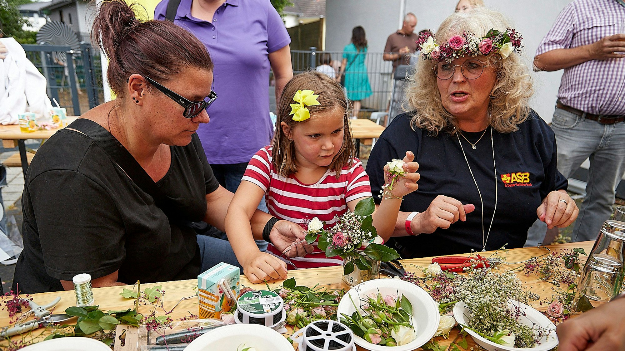 Zwei Frauen und ein Mädchen basteln Blumenkränze fürs Haar.