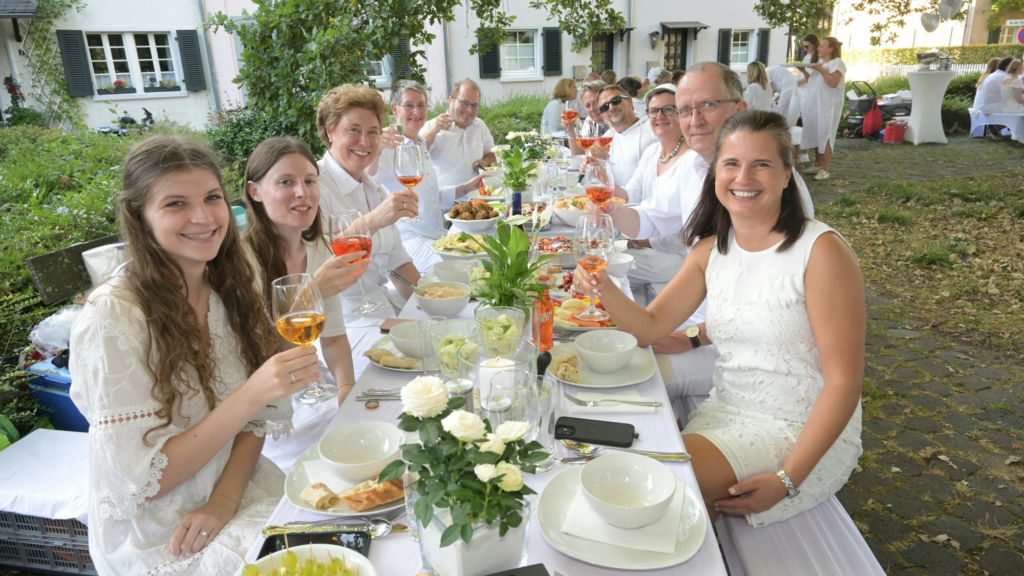 Menschen in weißer Kleidung sitzen an einem langen Tisch.