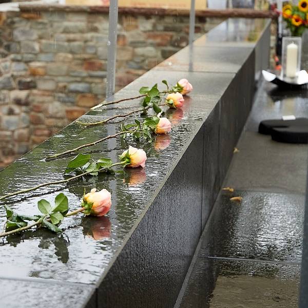 Fünf Rosen liegen als Symbol für die Opfer, die die Flutkatastrophe in Bad Münstereifel gefordert hat, auf einer regennassen Mauer.