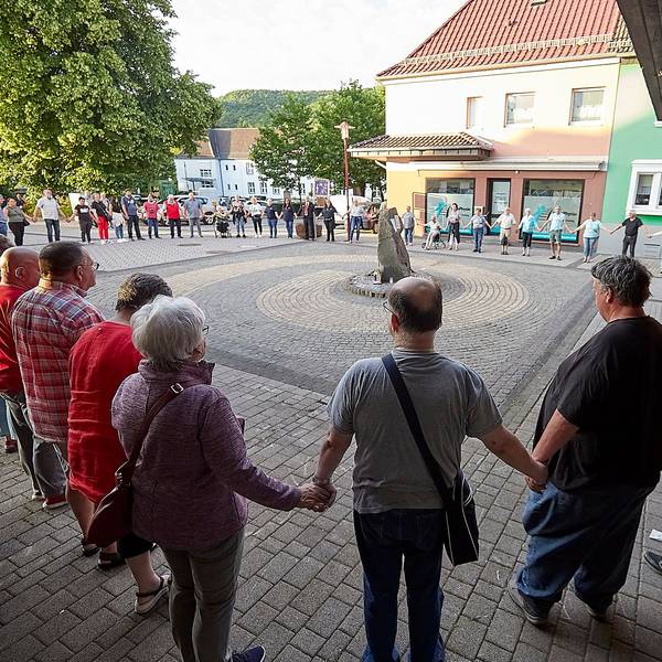 Zahlreiche Menschen stehen in einem großen Kreis um einen Stein. Sie halten sich zum stillen Gedenken an den Händen.