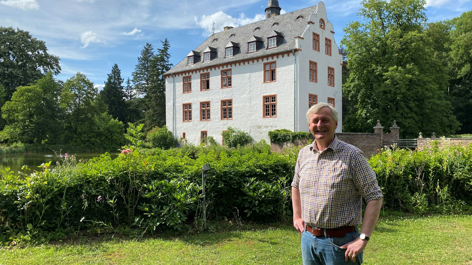 Ein Mann steht in einem Garten vor einem herrschaftlichen Haus.