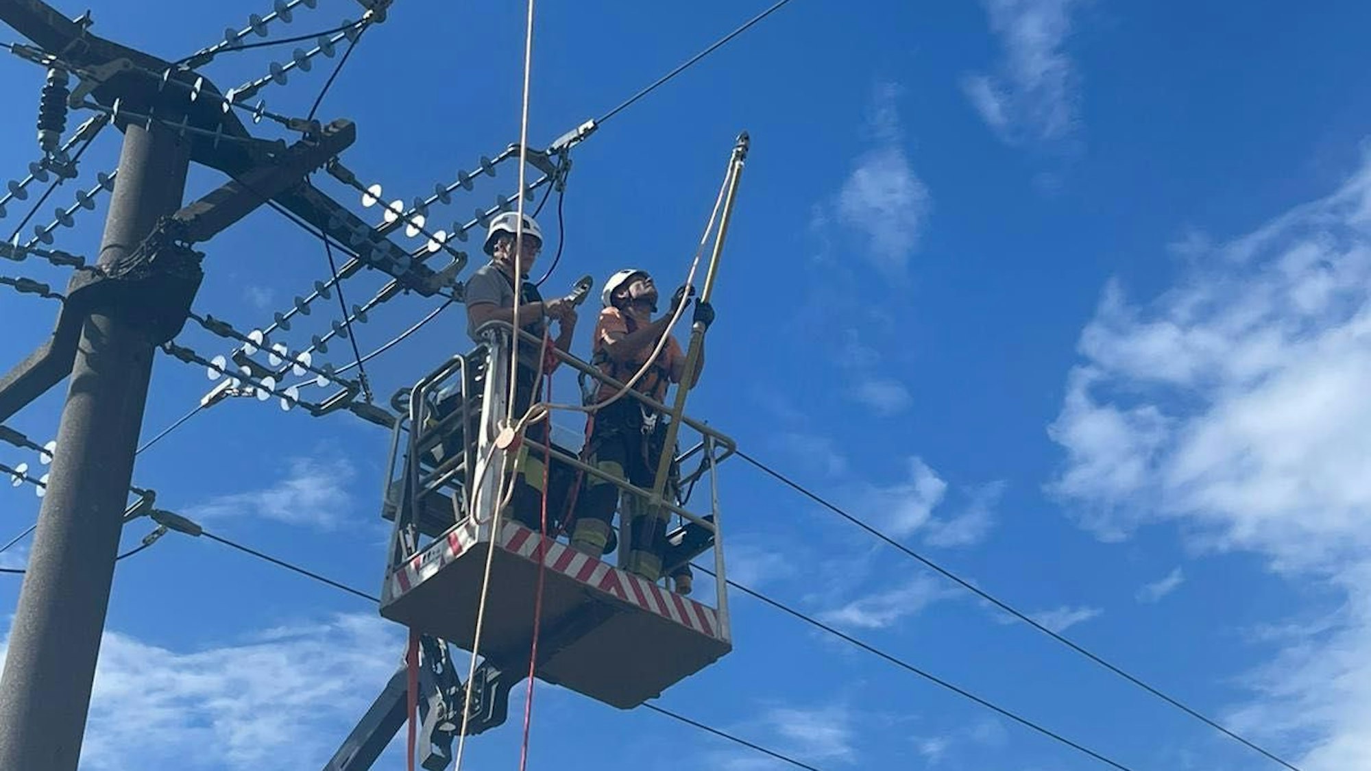 Monteure stehen in einem Hubwagen und arbeiten an einer Stromleitung.