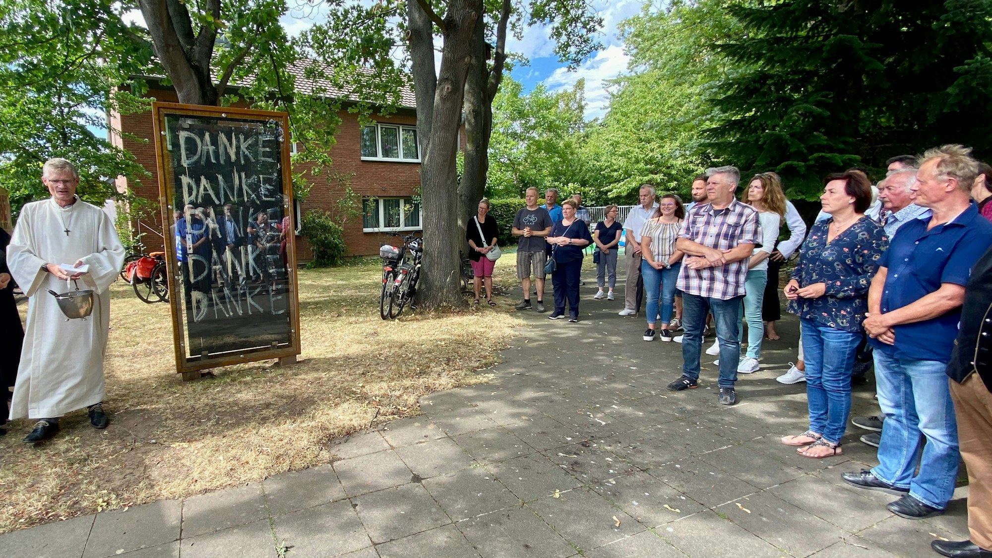 Ein Priester segnet zwei Türen, Besucher schauen zu.