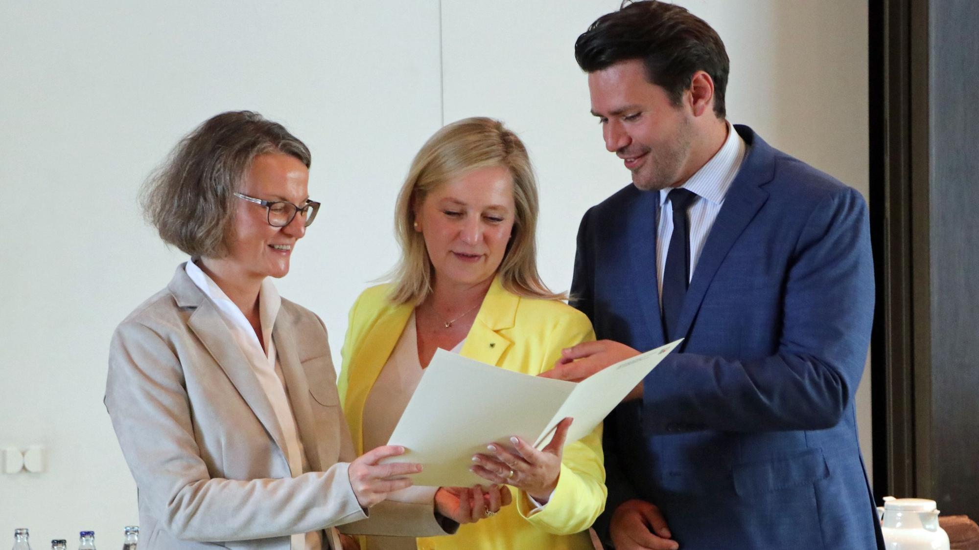 Das Foto zeigt drei Personen, die auf ein Dokument schauen.