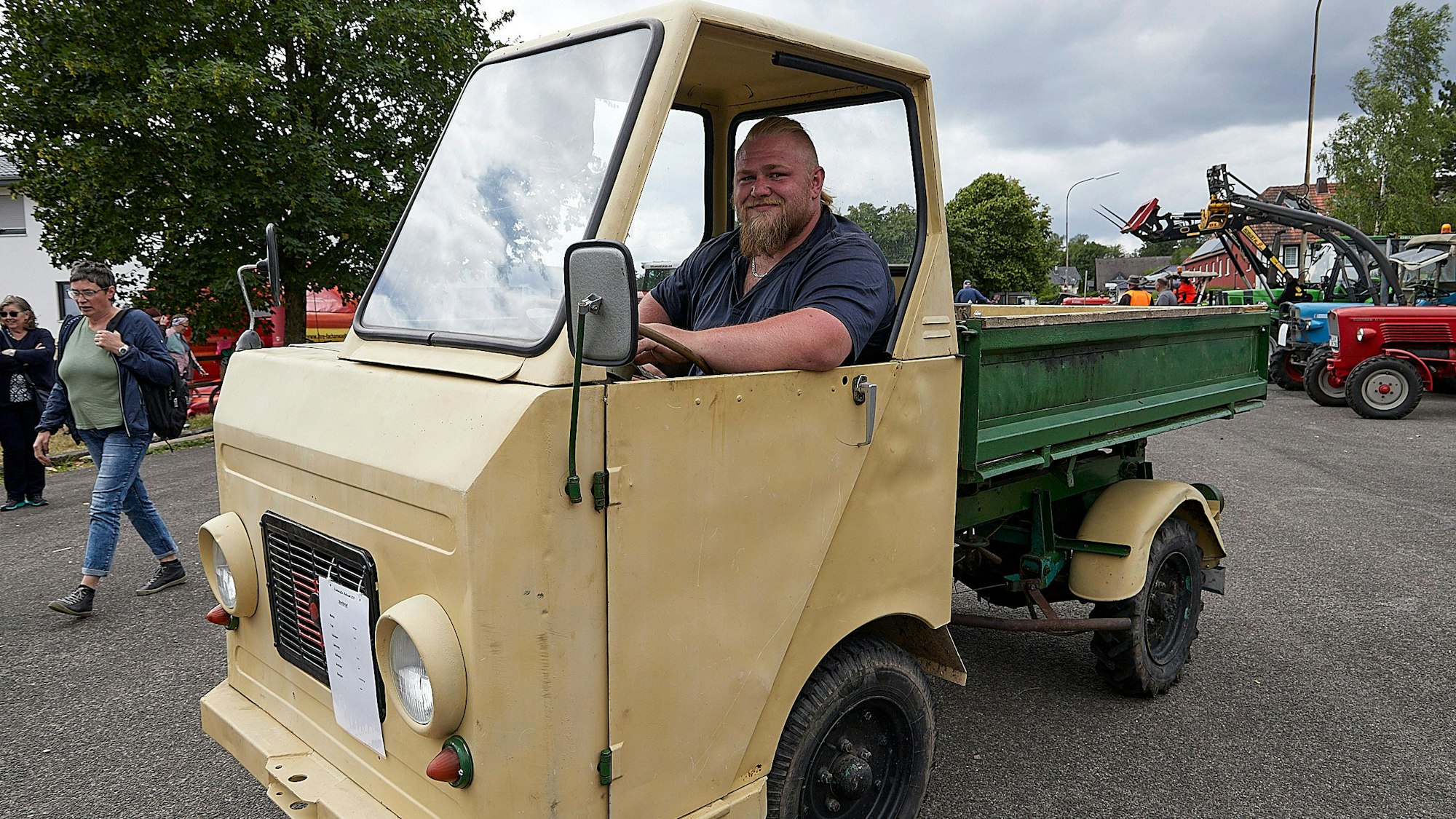 Ein Mann sitzt in einem beigen Muliticar mit grüner Ladefläche. Es ist ein kleiner Lkw, der in der damaligen DDR gebaut wurde.