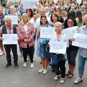 Zahlreiche Menschen stehen zusammen. Einige halten großformatige Spendenschecks in die Höhe.