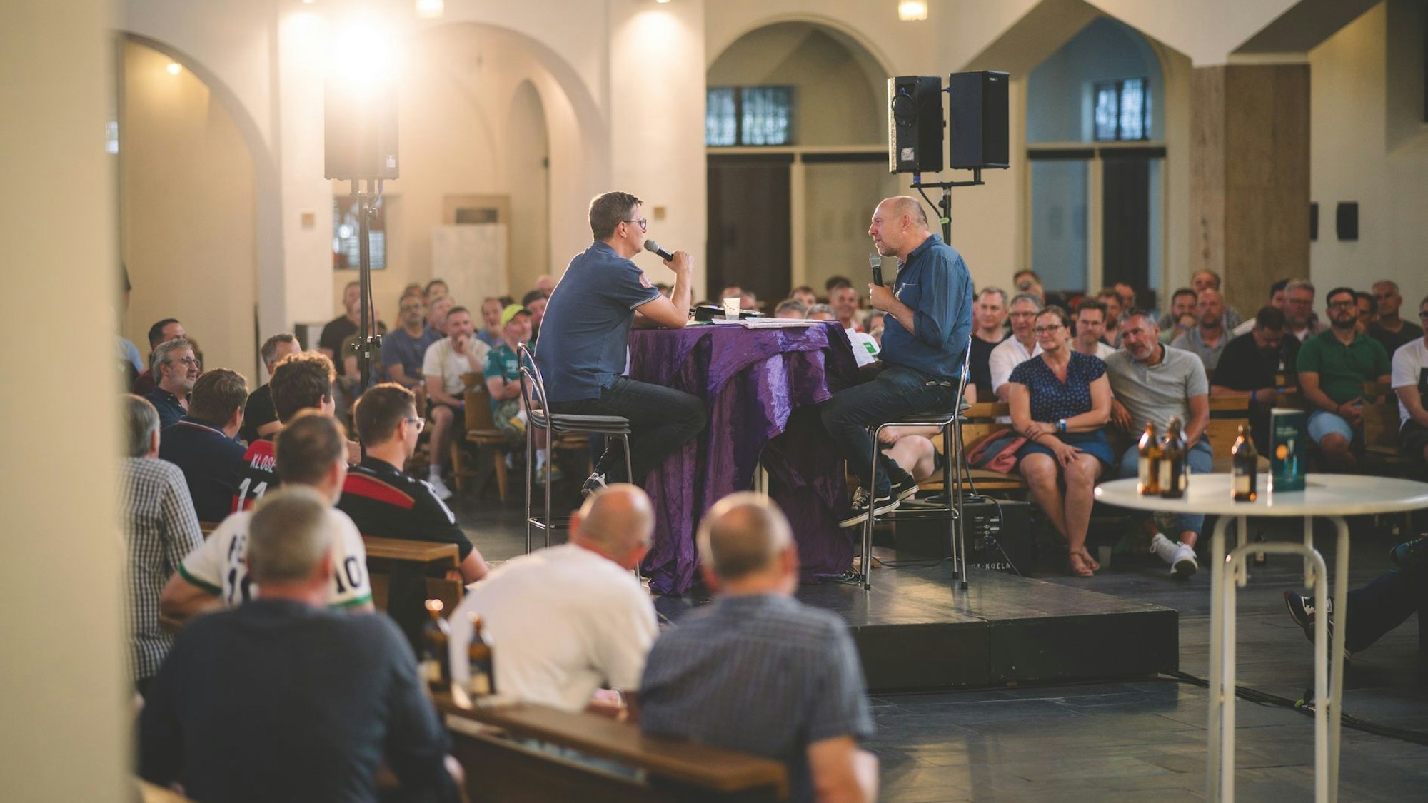 Um ein Podium in der Kirche herum sitzen viele Menschen.