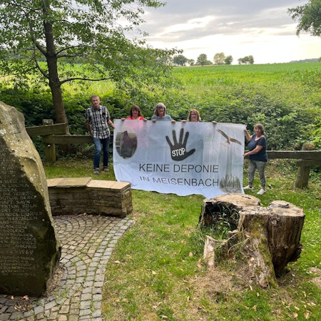 Fünf Menschen stehen mit einem Protestbanner auf einer Wiese.