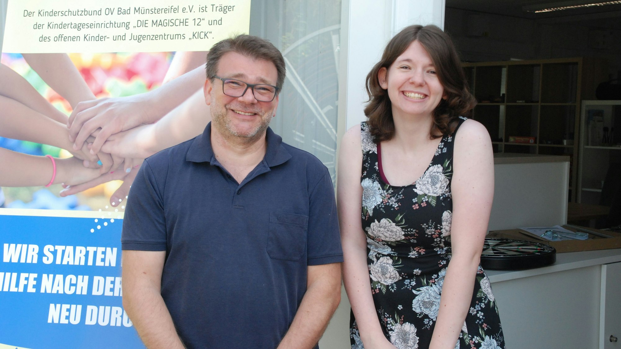 Ein Mann und eine Frau stehen neben einem Plakat am Eingang zum Jugendtreff Kick in Bad Münstereifel.