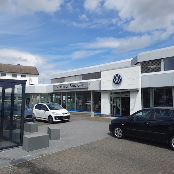 Der Eingang des Autohaus Badziong, drei Autos stehen davor auf dem Platz.