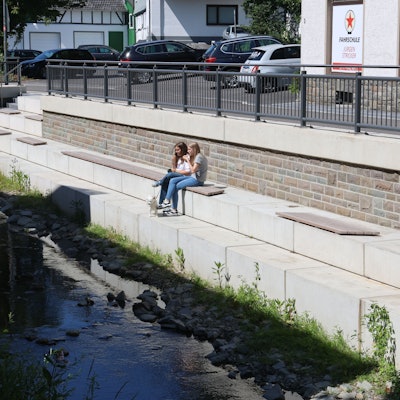 Zwei Mädchen sitzen an einer neu gestalteten Uferpromenade.