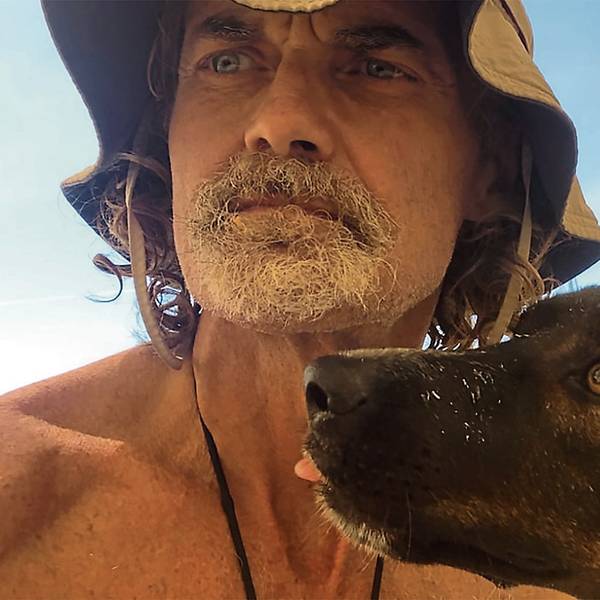 Ein bärtiger Mann und ein Hund vor einem Segel