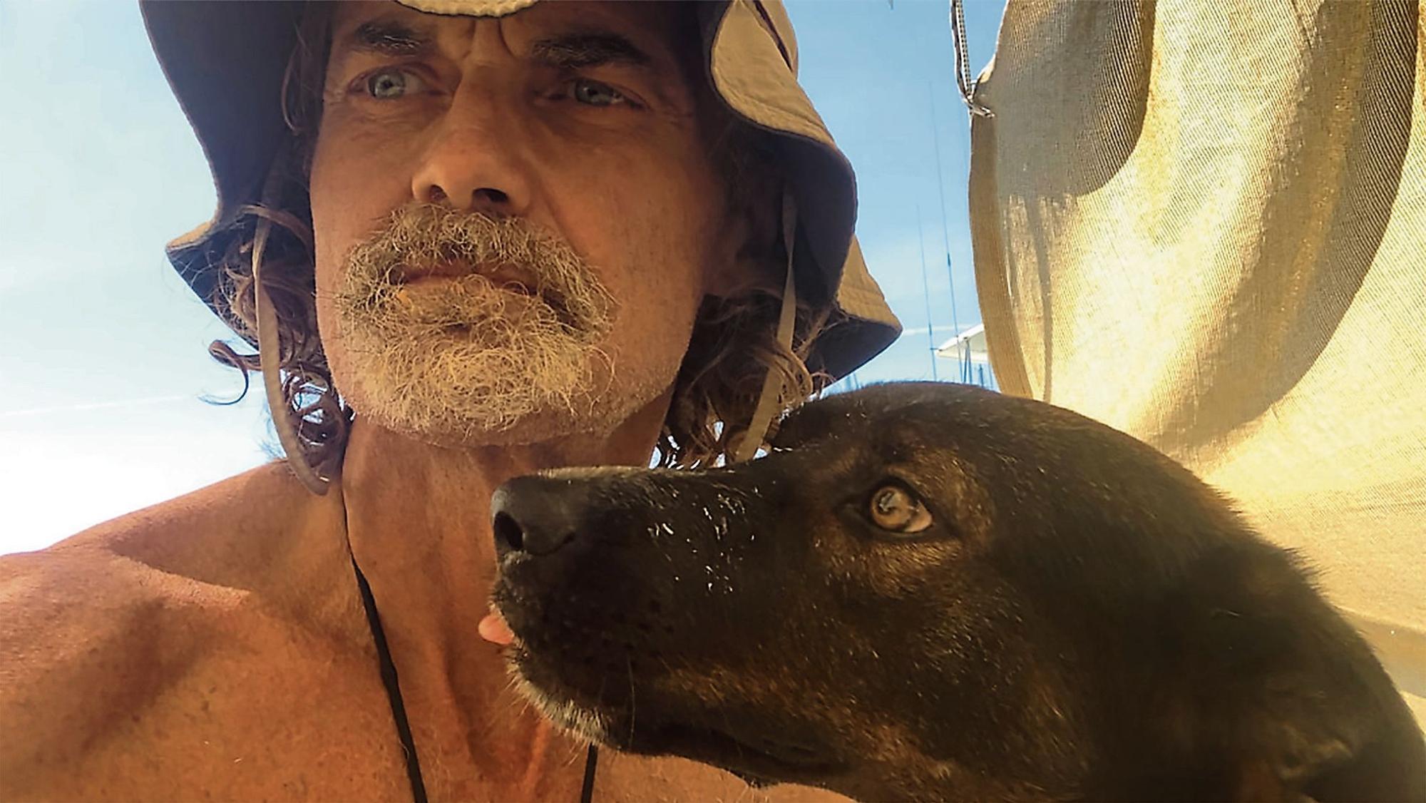 Ein bärtiger Mann und ein Hund vor einem Segel