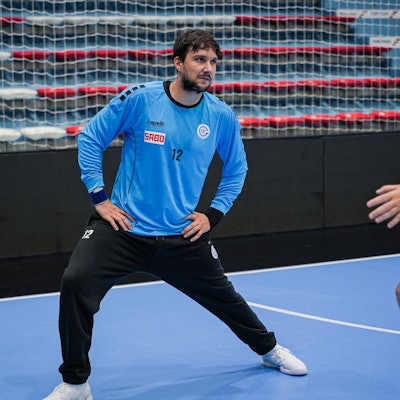 Ein Handball-Torhüter dehnt sich beim Training in einer Sporthalle.
