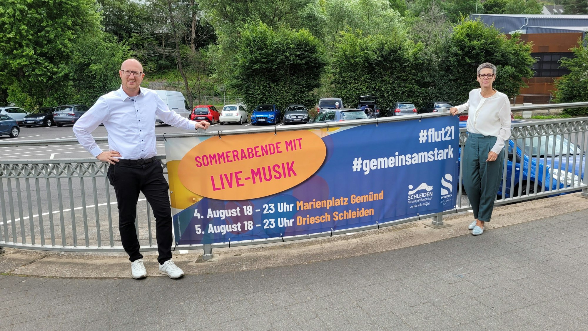 Bürgermeister Ingo Pfennings und Bianka Renn stehen neben einem Plakat, das auf das Helferfest hinweist.