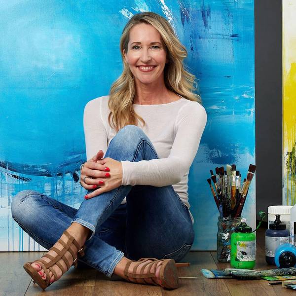 Die Künstlerin Susanne Herbold sitzt vor einer blau-gelben Leinwand, neben ihr stehen Farben und liegen Pinsel.
