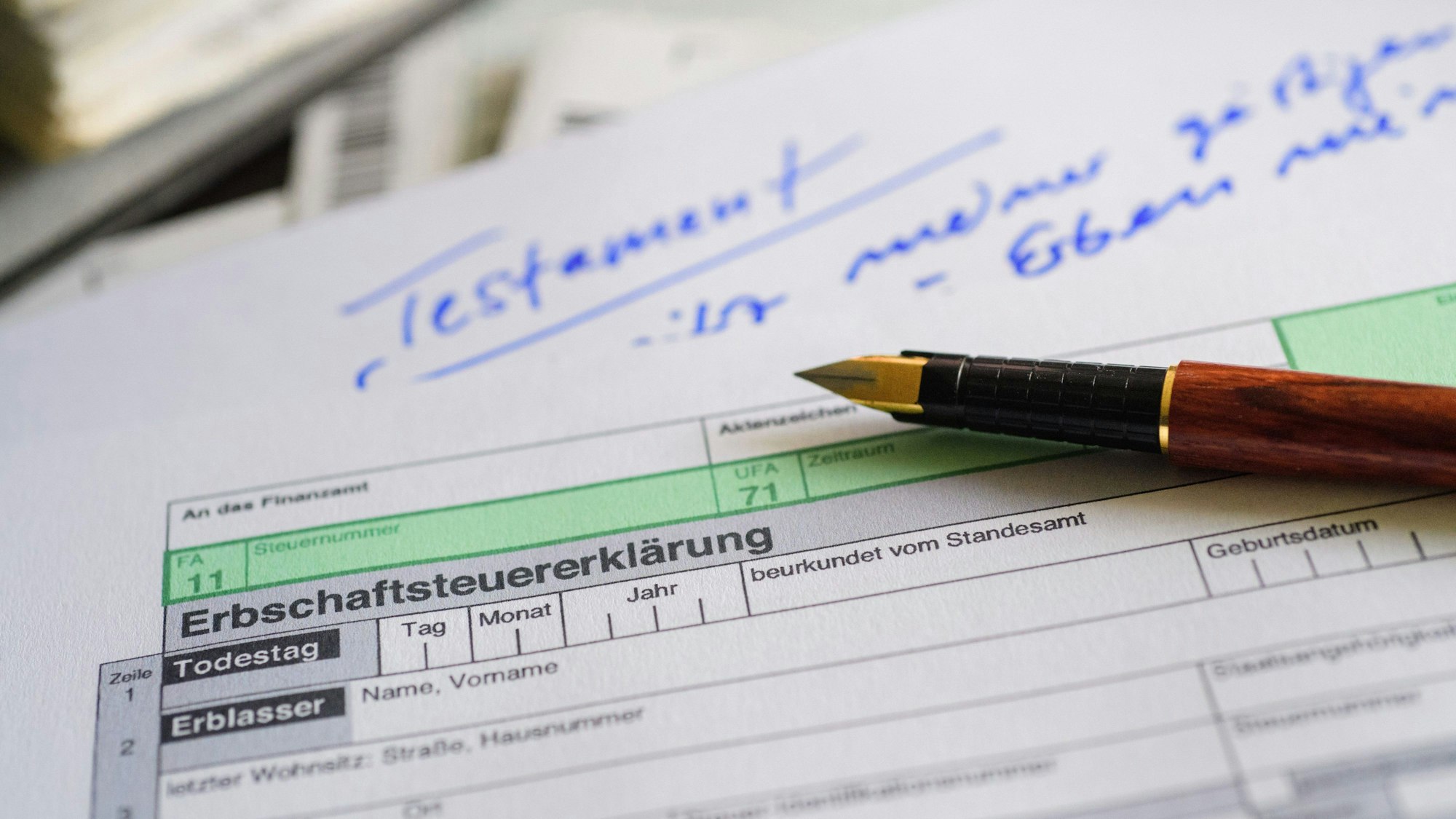 Ein Formular für die Erbschaftsteuererklärung sowie Stift und Testament liegen auf einem Tisch.
