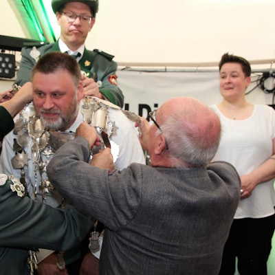 Schützen helfen Pastor Lambert Schäfer dabei, die schwere Königskette um den Hals von Christian Hartmann zu legen.