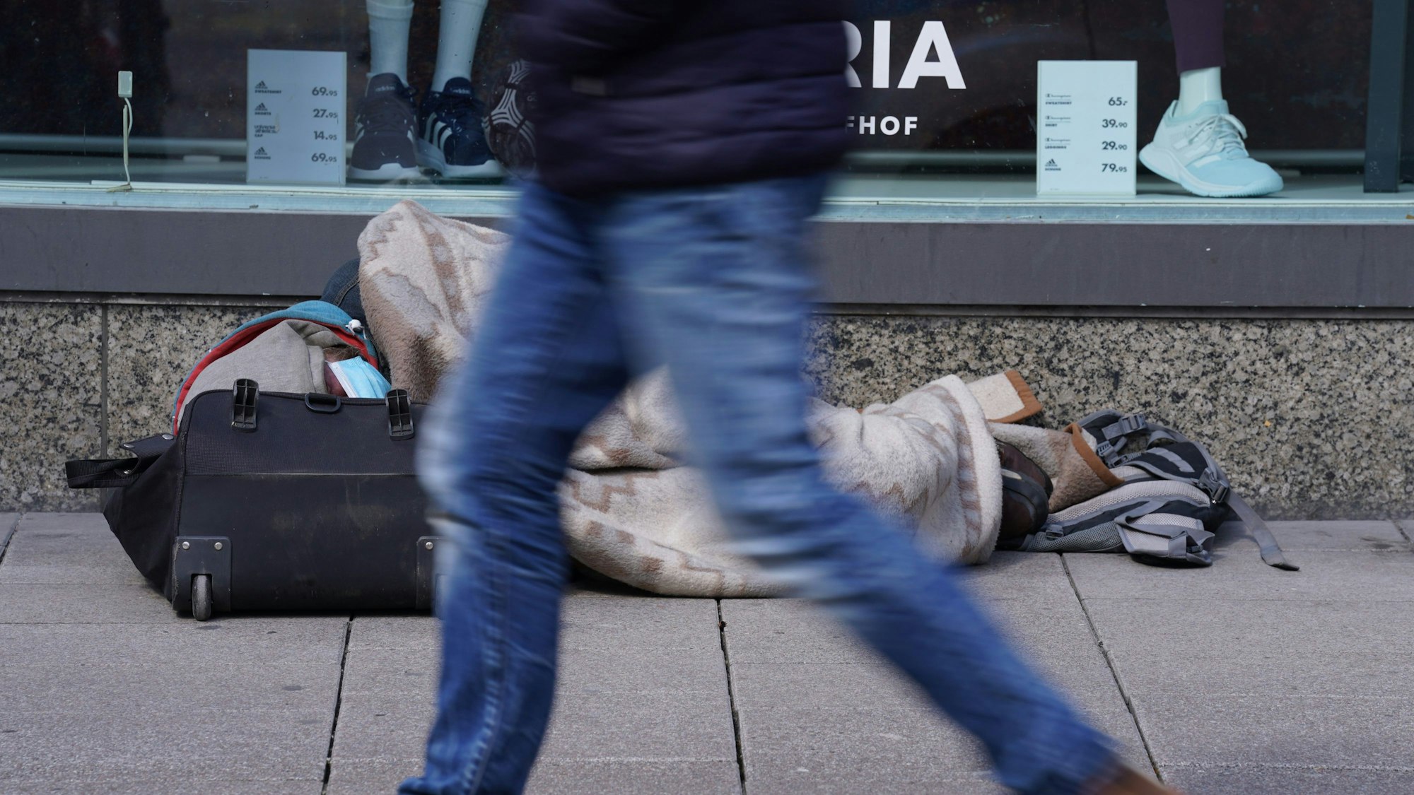 AEin Obdachloser liegt vor einem Schaufenster von Galeria Karstadt Kaufhof.
