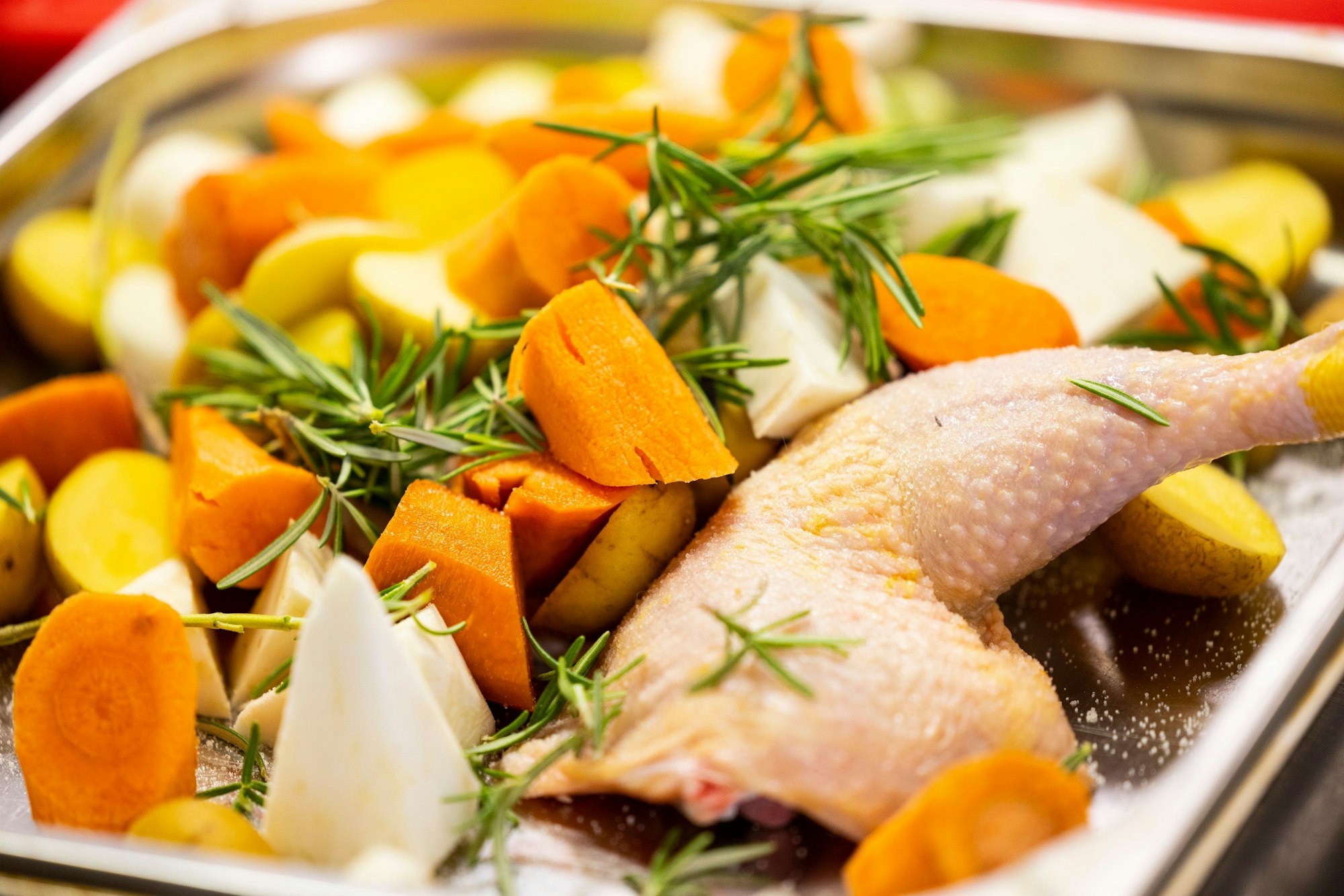 Die Hühnerkeulen kommen mit frischem Gemüse in den Ofen.