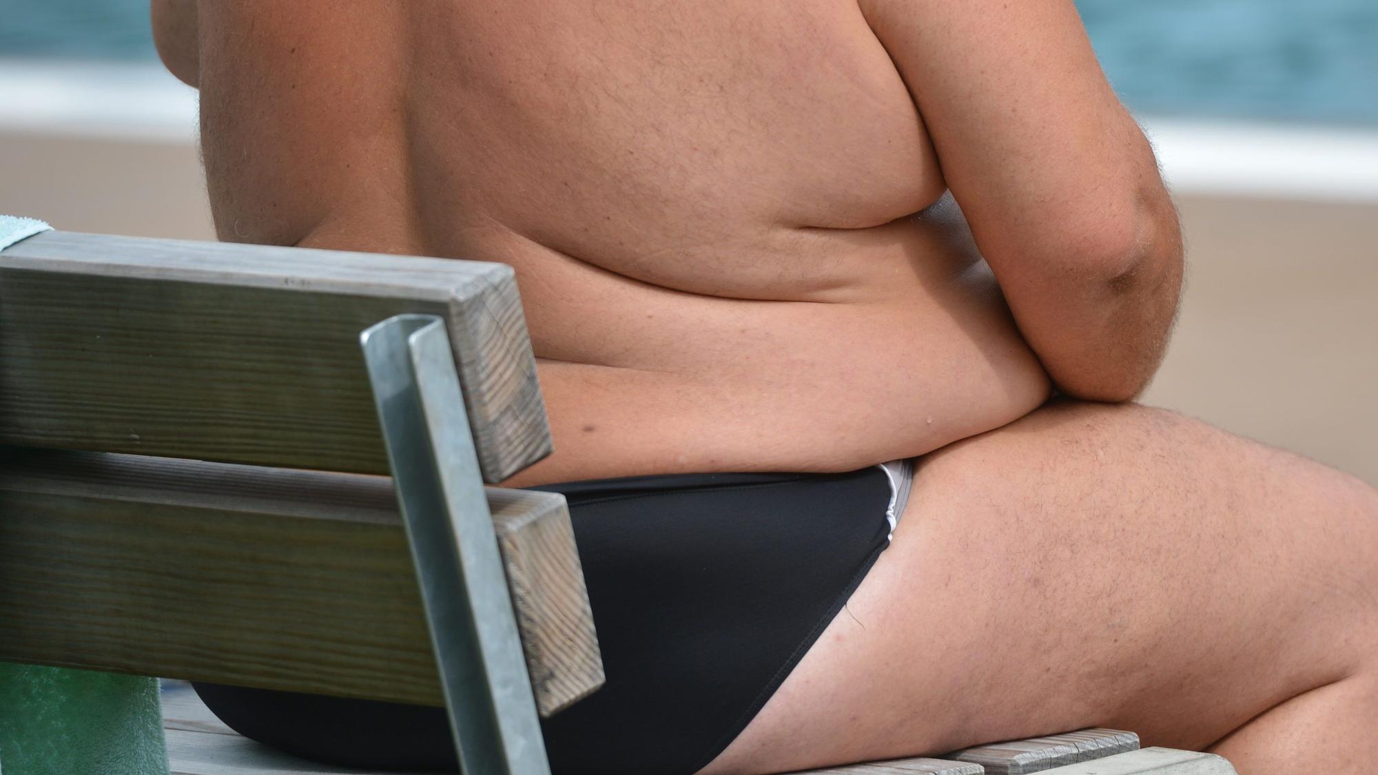 Ein übergewichtiger Mann sitzt in einem Freibad