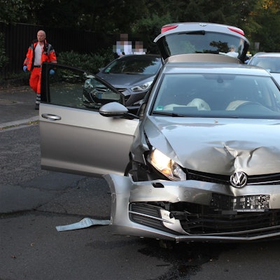 Ein VW mit verbeulter Motorhaube steht auf einer Straße. Im Hintergrund geht ein Rettungsdienstmitarbeiter.
