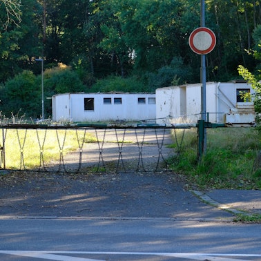 Auf einem mit einer Schranke gesicherten Gelände stehen abrissreife Notunterkünfte.