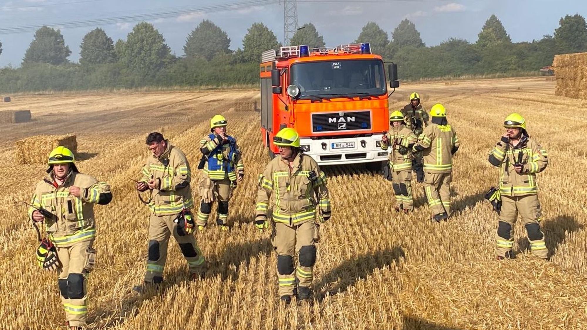 Das Bild zeigt mehrere Feuerwehrkräfte auf einem Stoppelfeld.