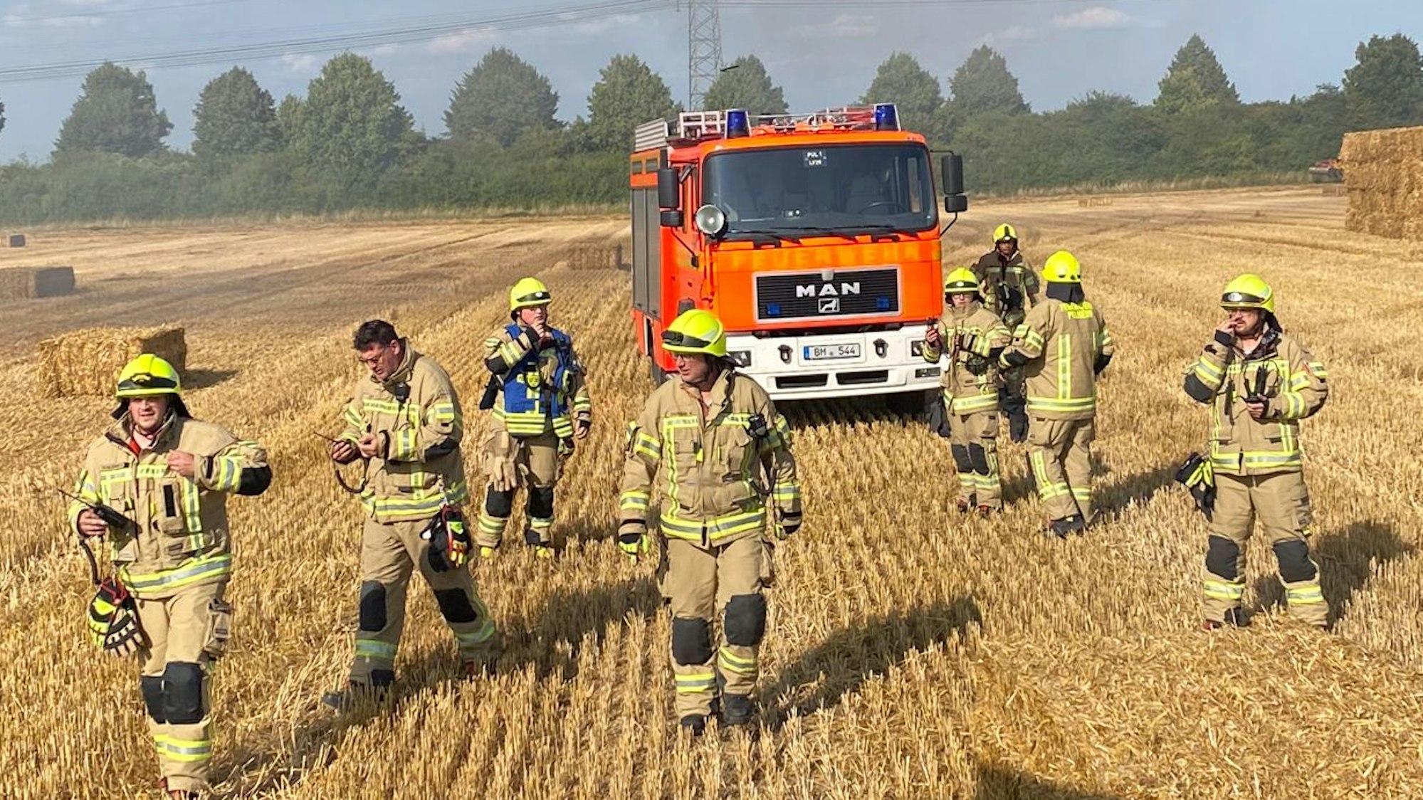 Das Bild zeigt mehrere Feuerwehrkräfte auf einem Stoppelfeld.