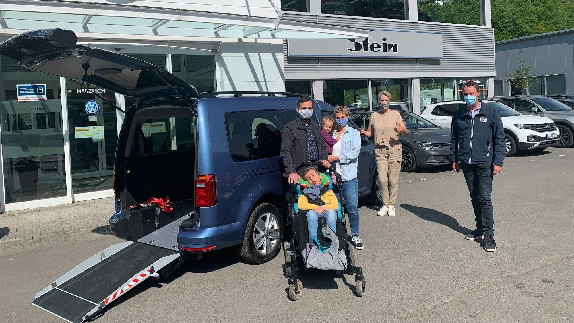 Mehrere Männer und Frauen sowie ein Kind im Rollstuhl haben sich vor einem rollstuhlgerechten Auto versammelt.