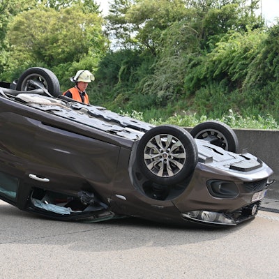 Das Bild zeigt einen auf dem Dach liegenden Wagen und mehrere Rettungskräfte auf der Fahrbahn.