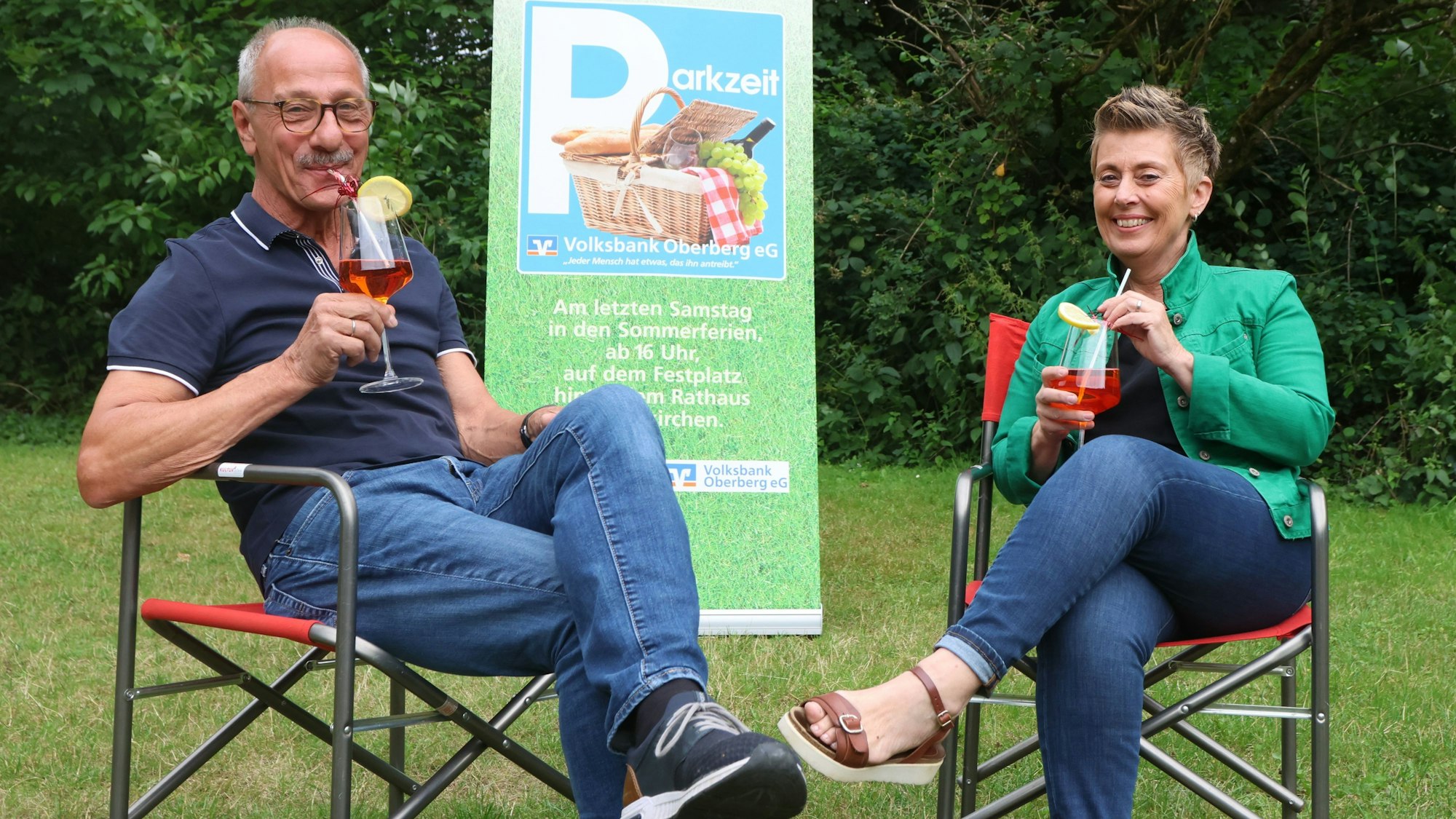 Ein Mann und eine Frau sitzen in Campingstühlen auf der Wiese und trinken Cocktails.