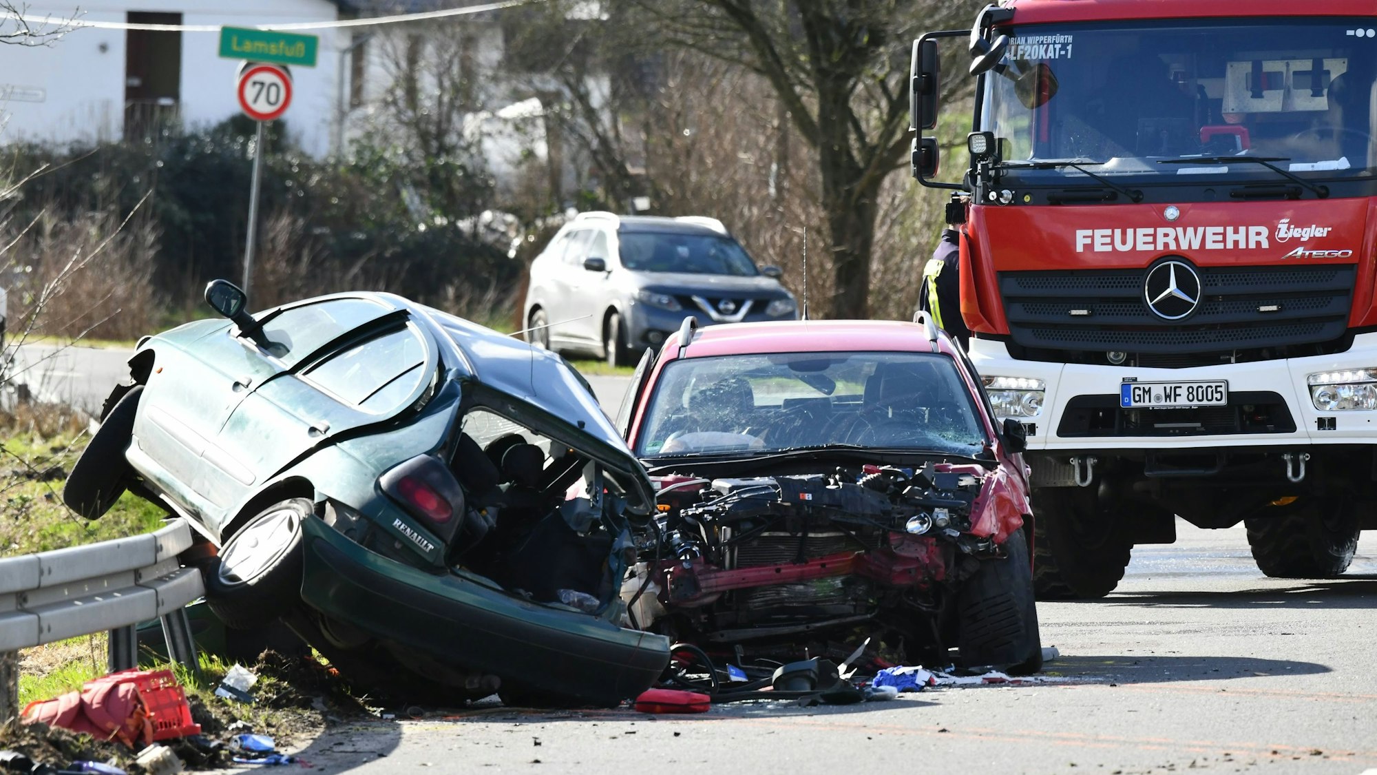 Zwei schwer beschädigte Kleinwagen stehen nach einem Unfall auf der Bundesstraße 506 bei Wipperfürth, im Hintergrund ein Feuerwehrfahrzeug und das Ortsschild von Lamsfuß.