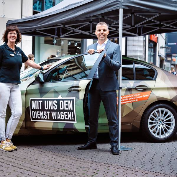 Nicole Venn und Thorsten Roth stehen vor einem in Tarnfarben folierten PKW auf der Schildergasse.