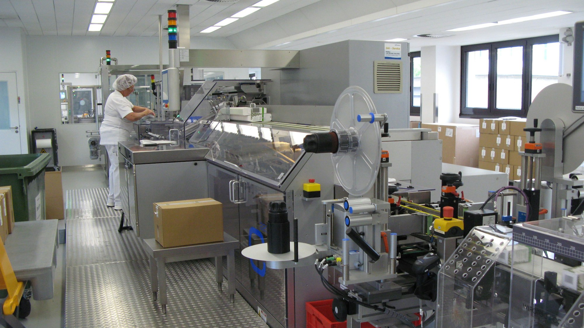 Eine Produktionsstraße und eine weiß gekleidete Frau mit Haube an einer Maschine.