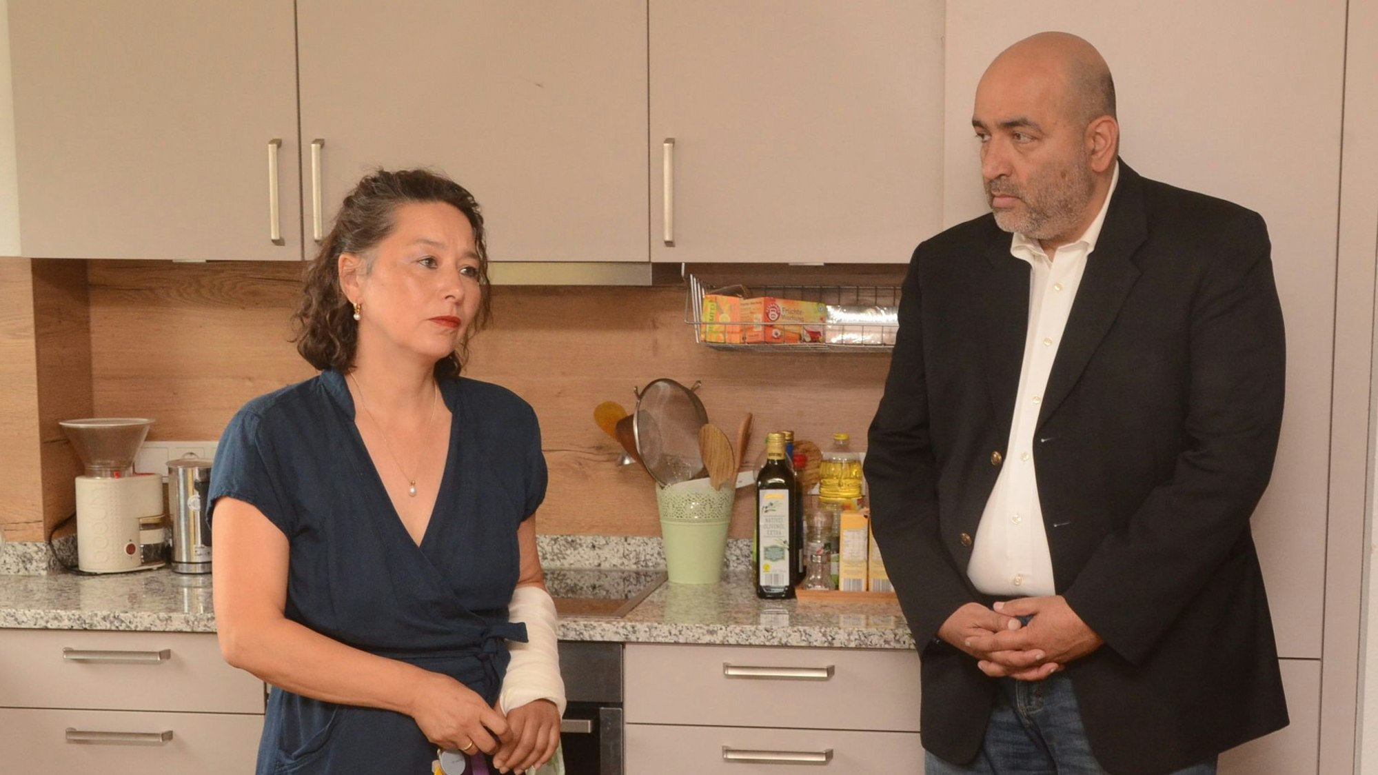 Eine Frau und ein Mann stehen in der Küche des Frauenhauses. Die Frau berichtet dem Mann von ihrer Arbeit.