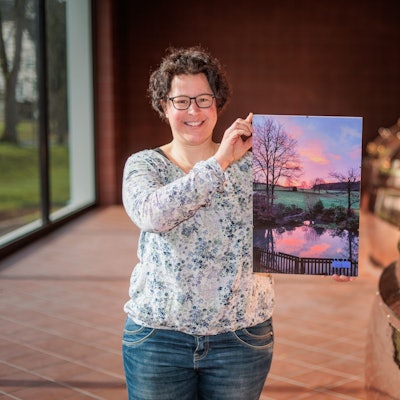 Eine Frau hält ein Foto eines Teiches im Sonnenaufgang in den Händen.