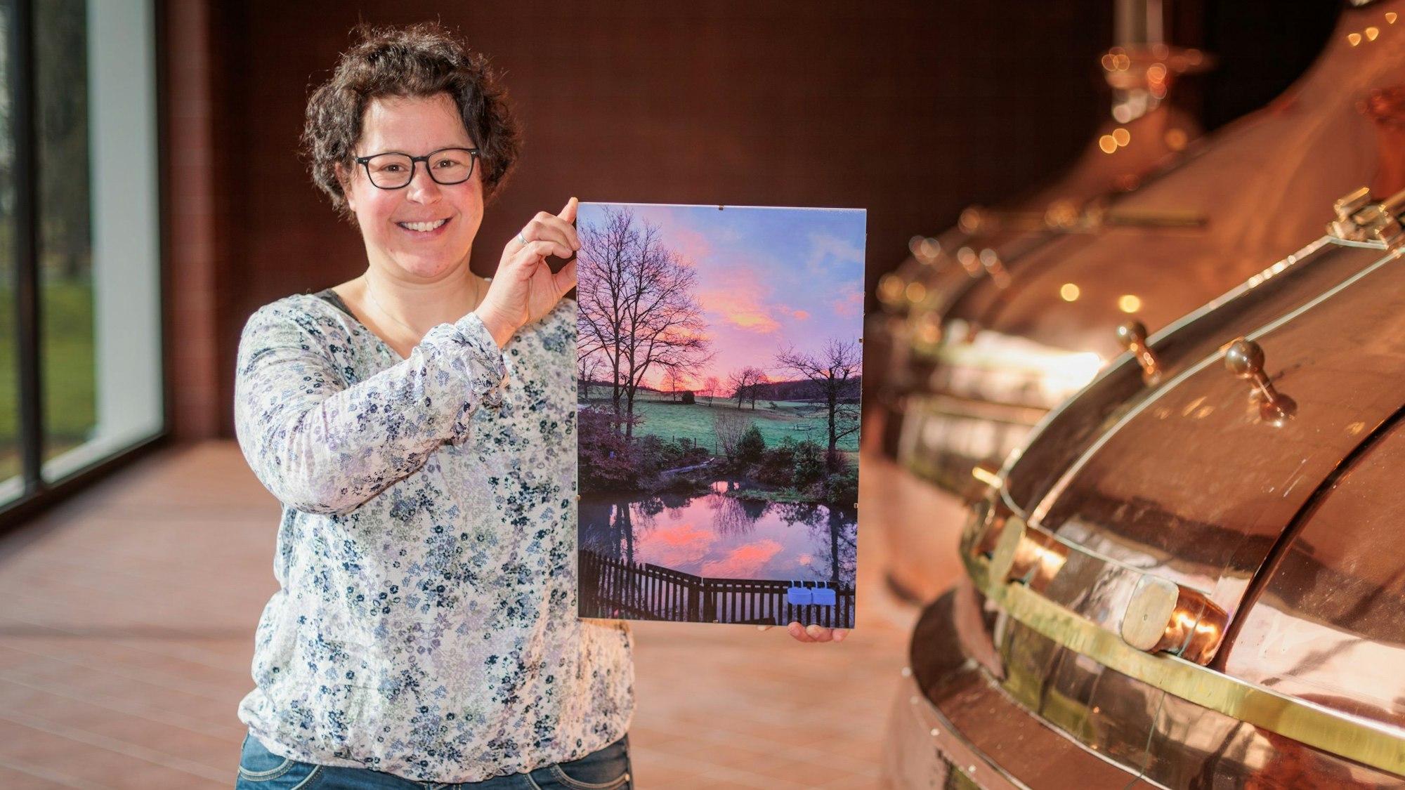 Eine Frau hält ein Foto eines Teiches im Sonnenaufgang in den Händen.
