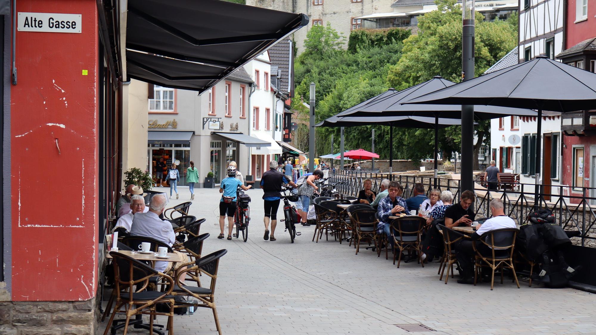 Das Bild zeigt die Fußgängerzone Werther Straße in Bad Münstereifel und Menschen, die draußen an den Tischen der Restaurants sitzen.