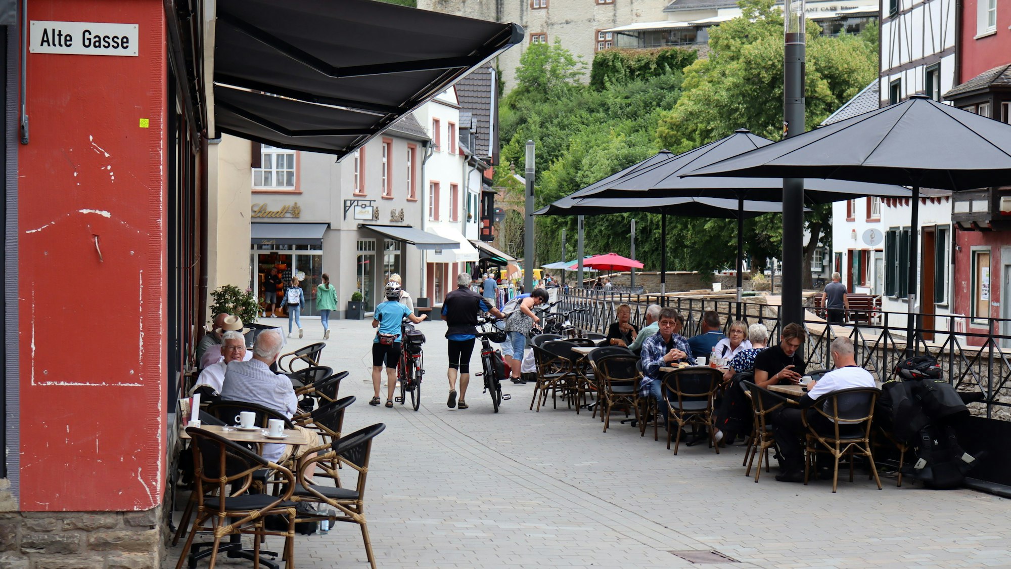 Das Bild zeigt die Fußgängerzone Werther Straße in Bad Münstereifel und Menschen, die draußen an den Tischen der Restaurants sitzen.