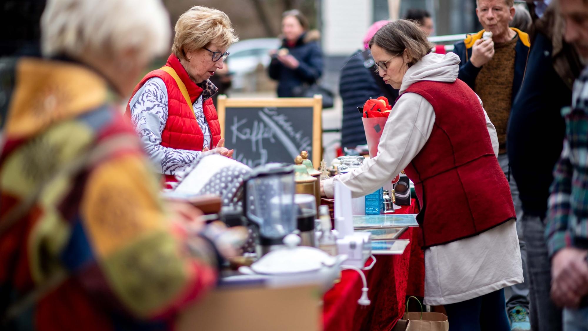 Das Bild zeigt einige Besucher des Trödelmarkts. Sie stöbern durch die angebotenen Artikel.