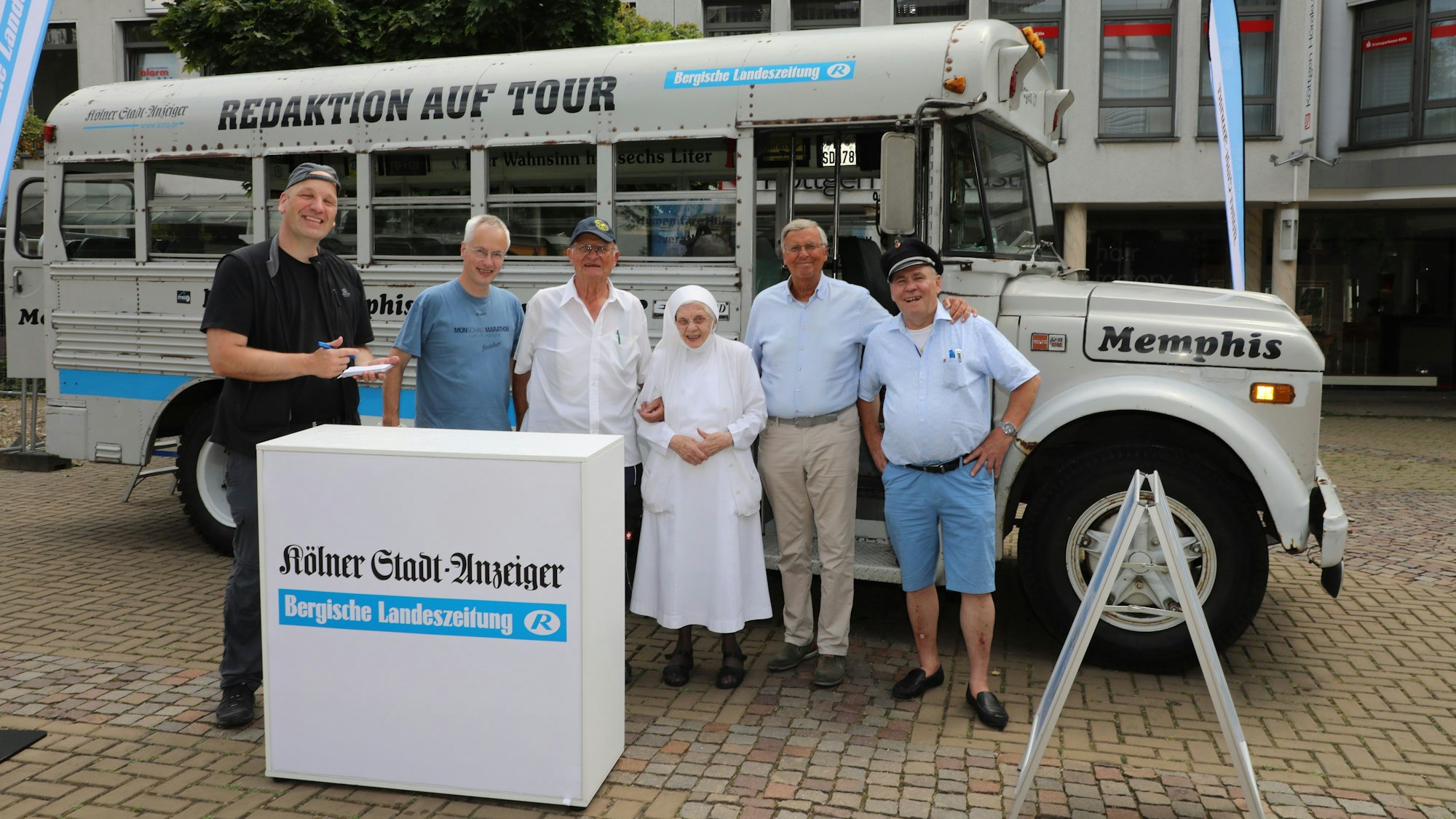 Menschen stehen hinter einem Tresen vor einem historischen amerikanischen Schulbus.