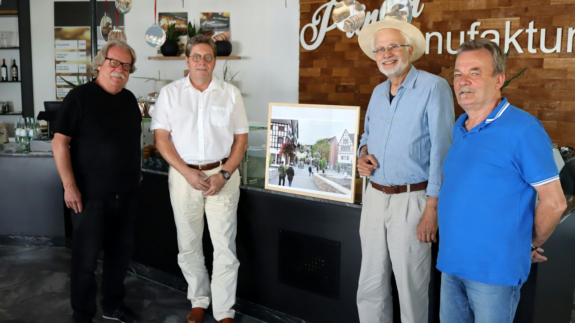 Auf dem Bild sind vier Männer zu sehen. In ihrer Mitte haben sie ein Foto mit einer Ortsansicht von Bad Münstereifel.