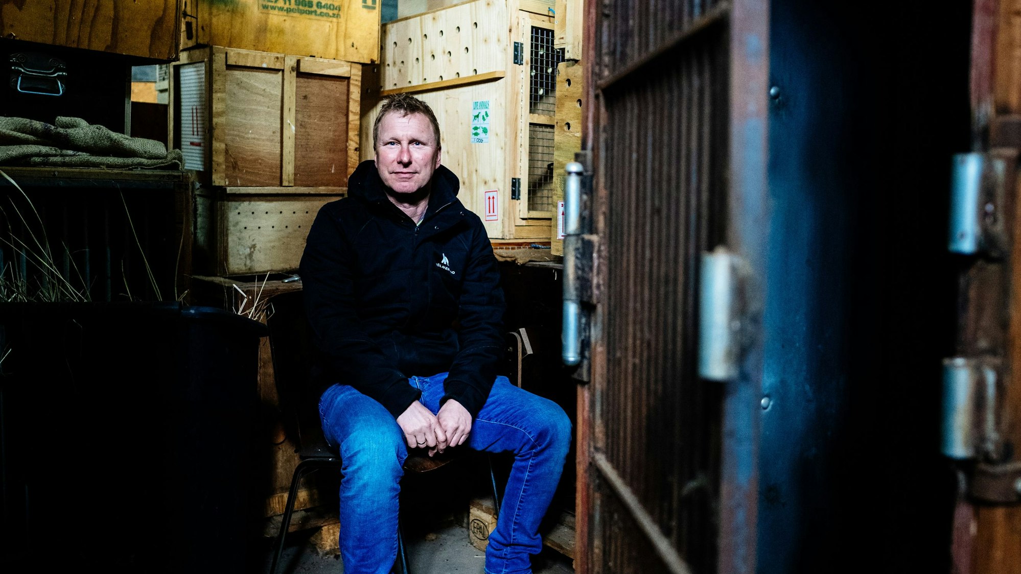 Säugetiere, Vögel und Reptilien brauchen zu ihren Verhaltensweisen und ihrer Größe passende Transportboxen. Kurator Bernd Marcordes muss „an alles denken und lernt immer Neues dazu“. Marcordes sitz in blauer Jeans und schwarzem Sweater inmitten von ganz unterschiedlichen Transportkisten.