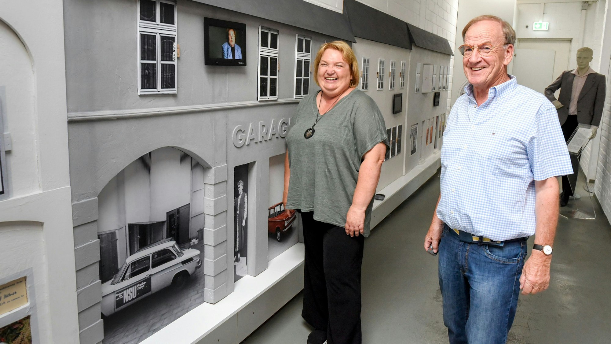 Eine Frau und ein Mann stehen vor einer Kulisse, die historische Gebäude zeigt.