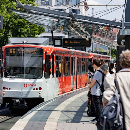 Menschen stehen in Bonn am Gleis. Gerade fährt die Linie 66 Richtung Bad Honnef ein.