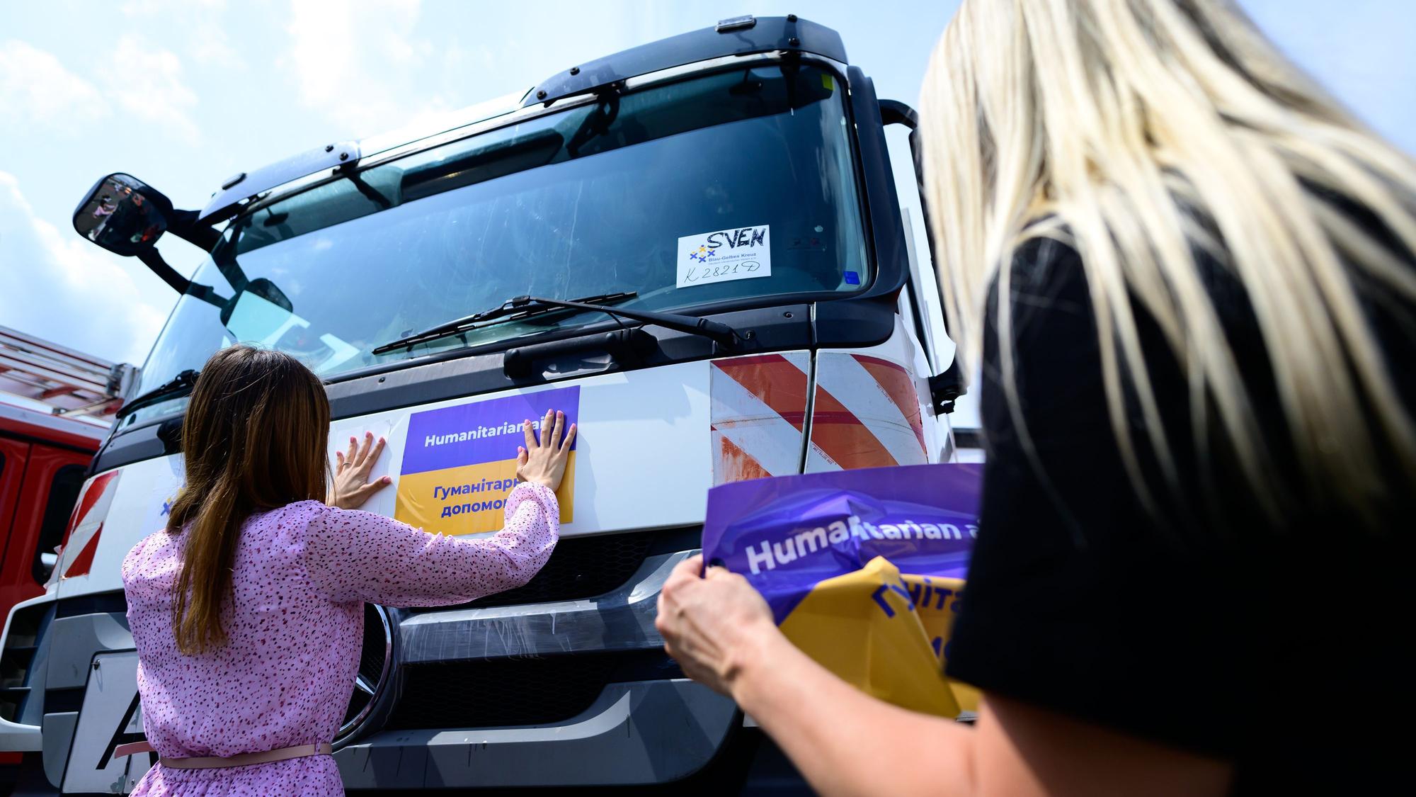 Eine Frau klebt einen Aufkleber auf ein Spezialfahrzeug, das in die Ukraine gefahren wird.