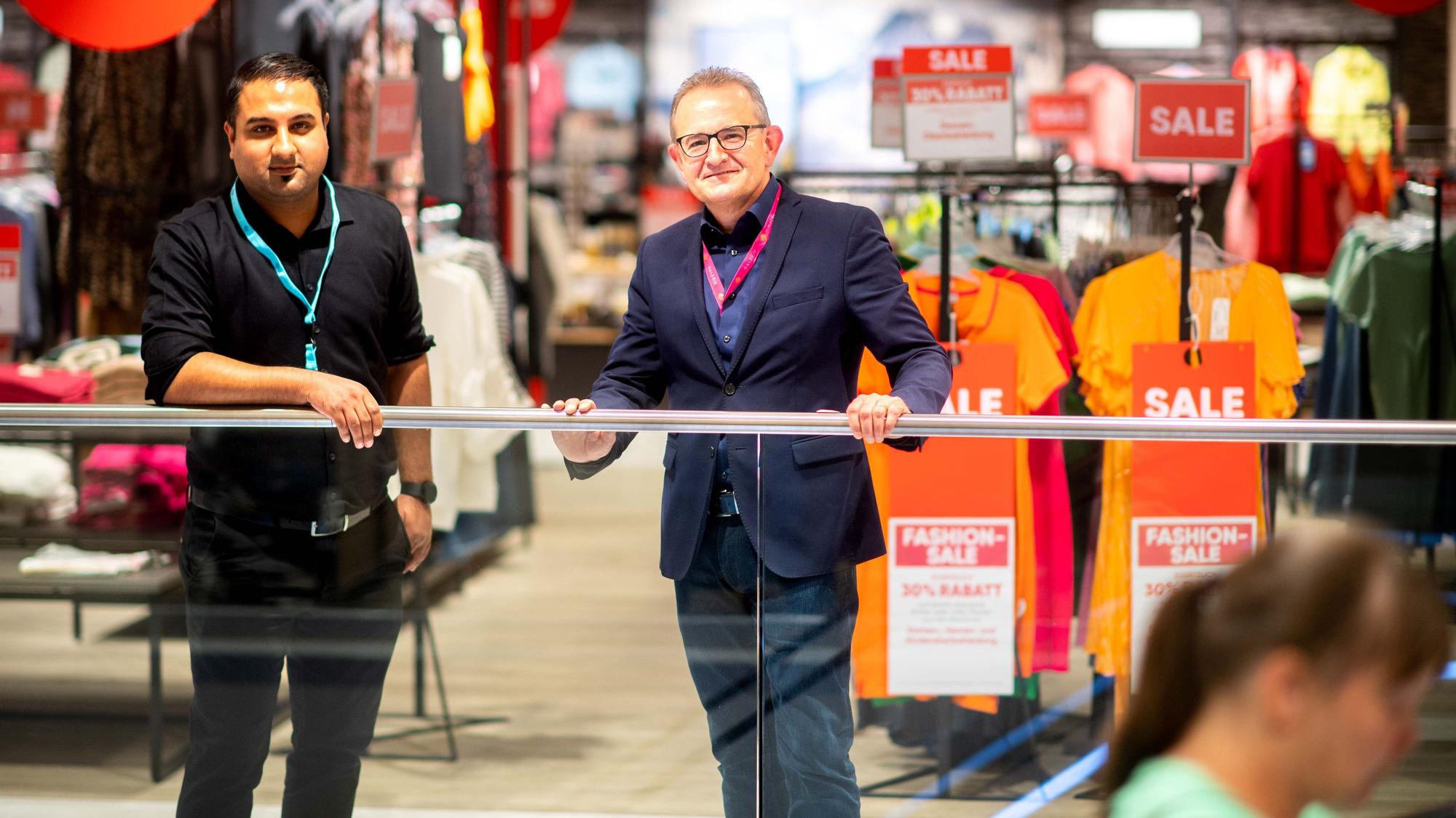 Der neue und der alte Chef der Galeria-Filiale stehen am Geländer.