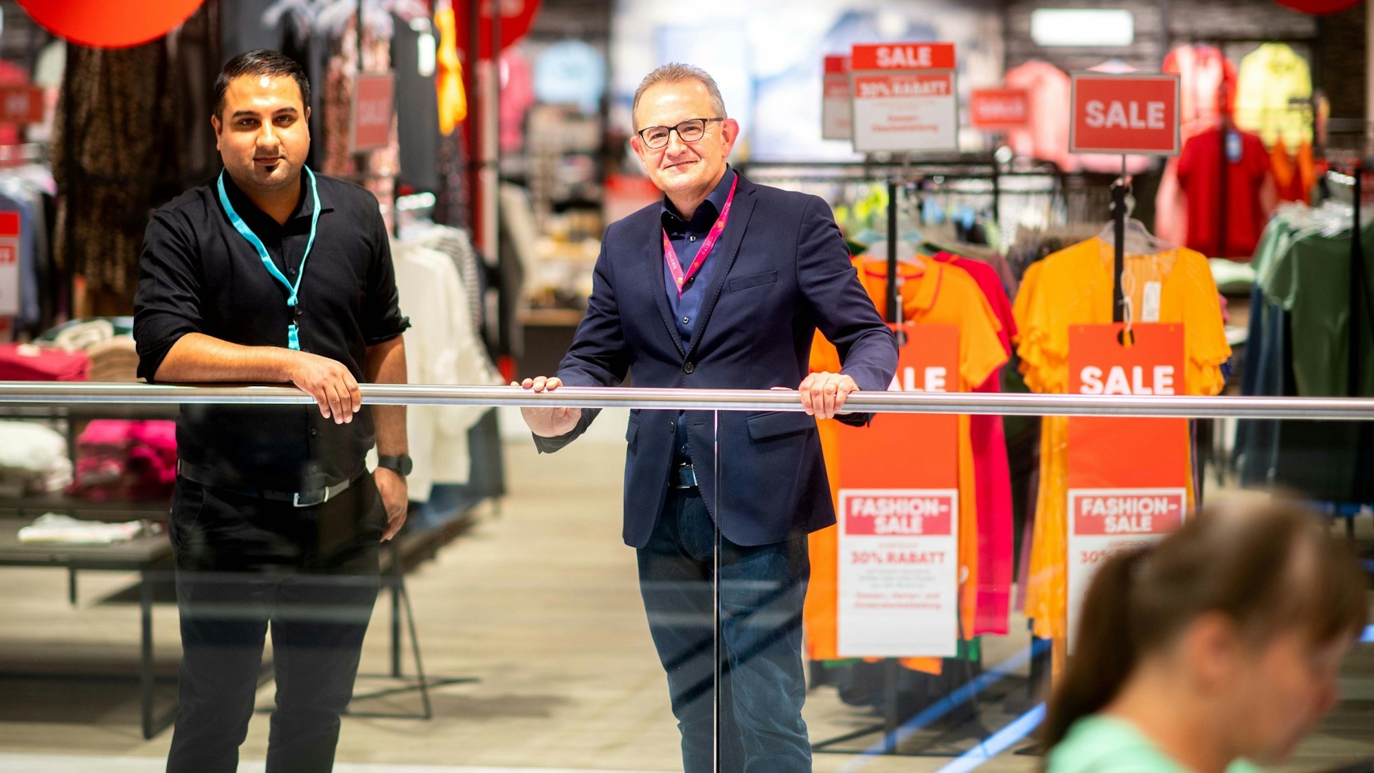 Der neue und der alte Chef der Galeria-Filiale stehen am Geländer.